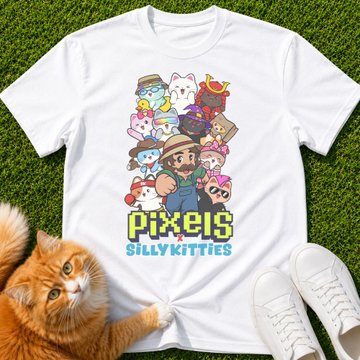 White t-shirt displayed on grass featuring 'PIXELS SILLY KITTIES' artwork with pixel-style cartoon characters and an orange cat lying beside it.
