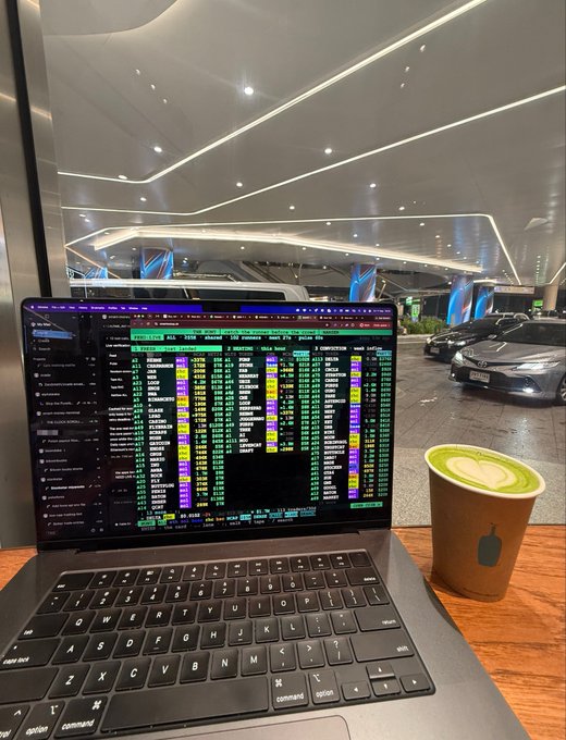 A trader enjoys a matcha latte while monitoring real-time stock data across multiple watchlists—including the NYSE, Asia, Europe, and Crypto sectors—on a MacBook at a modern airport lounge, capturing the relaxed yet vigilant mindset of "smart money and chill."