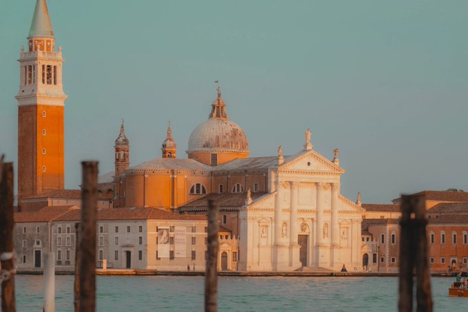A scenic view of Venice featuring the Church of San Giorgio Maggiore with its prominent dome and bell tower, viewed from across the water at sunset.