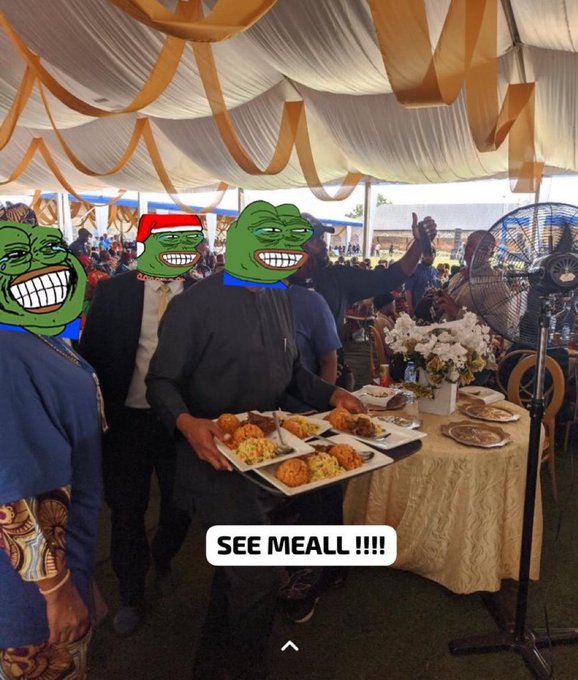 A photo from an outdoor event tent decorated with cream and gold drapery, featuring people whose faces have been edited with troll faces memes, with 'SEE MEALL !!!!' text overlay, and one person holding a tray of food.