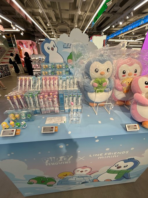 A retail display table showcases 'TINY PENGUINS x LINE FRIENDS minini' plush toys and stationery in a brightly lit store.