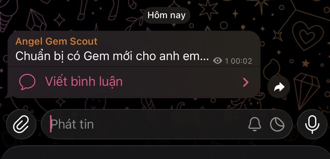 The image shows a message conversation between two people, with one person's name being "Anh" and the other person's name being "Em." The text of their conversation includes phrases such as "Gem mới sẽ công bố trong hôm nay," which translates to "I am thinking about you." This message is displayed on a phone screen, and the time shown in the image is 1:02.