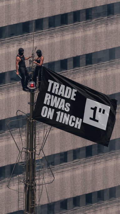 Two climbers in black masks scale an urban antenna structure to unfurl a large banner reading "TRADE RWAS ON 1INCH," promoting the 1inch crypto platform's real-world assets (RWAs) offerings in a bold guerrilla marketing stunt that complements the optimistic "GM" (good morning) crypto greeting.