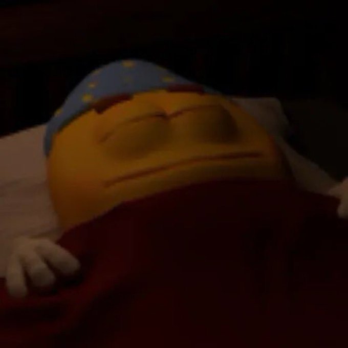 A dimly lit scene showing a yellow smiling cartoon character wearing a blue nightcap with yellow stars, sleeping under a red blanket.