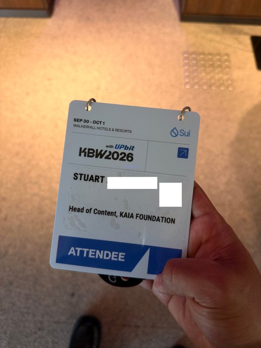 A hand holds an attendee badge for the KBW2026 conference (Sept 30-Oct 1, Walkerhill Hotels & Resorts), sponsored by Sui and Upbit, for Stuart, Head of Content at KAIA Foundation.