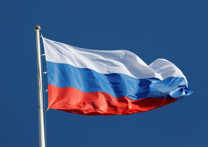 The Russian tricolor flag waves against a clear blue sky, symbolizing the nation behind the Bank of Russia's newly unveiled draft rules for officially regulated crypto trading. The image visually anchors the article's headline about Russia's push toward bringing digital assets under government oversight.