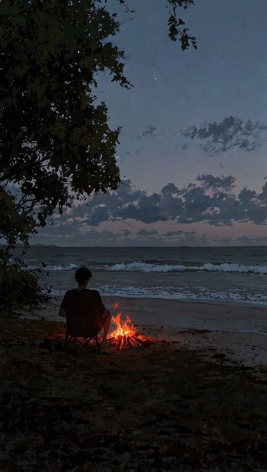 A serene, atmospheric night photograph of a silhouetted person sitting on a beach by a glowing campfire, looking out at the ocean under a dark, cloudy sky.