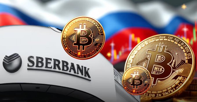 The image features the Sberbank logo alongside multiple golden Bitcoin coins, set against a backdrop of the Russian flag and a candlestick price chart, visually symbolizing Russia's largest bank embracing cryptocurrency like Bitcoin as collateral for loans.