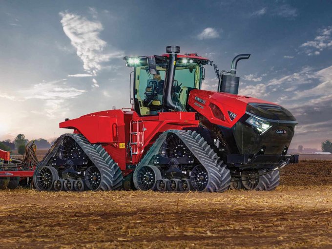 A large red Case IH tractor with quad tracks parked in a dirt field under a partly cloudy sky.