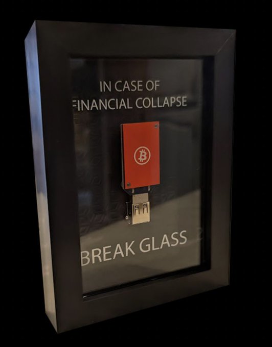 The image features a small black framed sculpture that reads "In case of financial collapse" with an orange button attached to it. The sculpture is made from composite fiberglass, giving it a unique and artistic appearance. The text "I Am GPIO Glass" suggests that this artwork may be related to Bitcoin or cryptocurrency in some way. The post about the sculpture also mentions that it was created by I Am GPIO, which could indicate that the artist's intention might have been to draw attention to the potential risks of financial collapse or to promote Bitcoin as a means of protection against such issues.