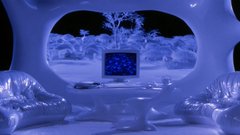 A futuristic, icy blue-toned room with curved walls and organic furniture, featuring a screen displaying an image in the center.