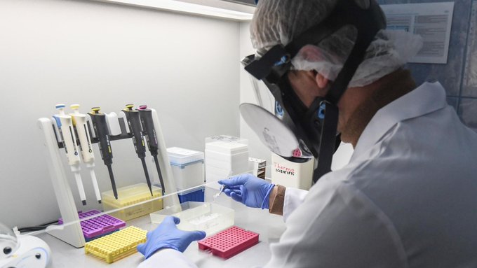 A lab worker wearing a hairnet, safety goggles, and blue gloves uses a multi-channel pipette to transfer samples into a multi-well plate, with a labeled box reading "SARS-CoV-2" visible on the bench. The image does not relate to the accompanying post, which contains only a wallet address and Chinese text unrelated to laboratory work.