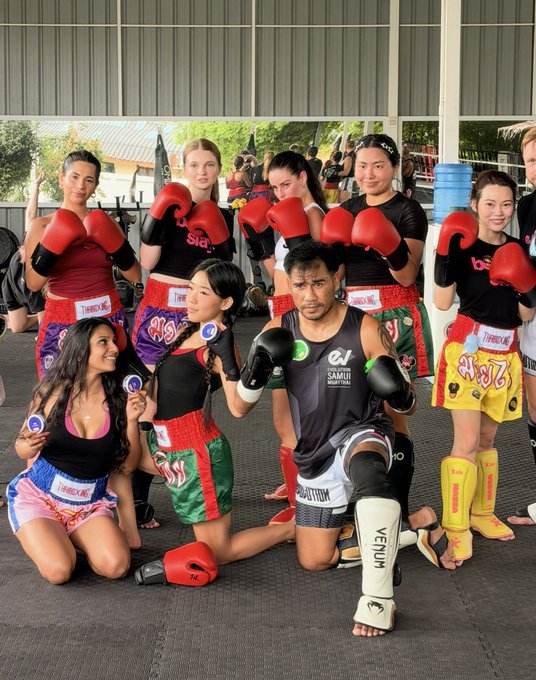 A group of women wearing red boxing gloves and colorful Muay Thai shorts (labeled "THBOC.MG") pose alongside a male trainer in Venum shin guards, all in fighting stances inside a training gym. The image ties into the post's "GM frens be nice to CT girls" caption by showcasing these tough, capable female fighters — a playful reminder that these women can clearly handle themselves in the ring.