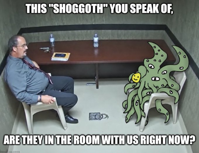 A meme showing a man in a gray shirt and tie sitting across from a digitally added green Cthulhu-like creature on a chair, with text reading 'THIS "SHOGGOTH" YOU SPEAK OF, ARE THEY IN THE ROOM WITH US RIGHT NOW?'