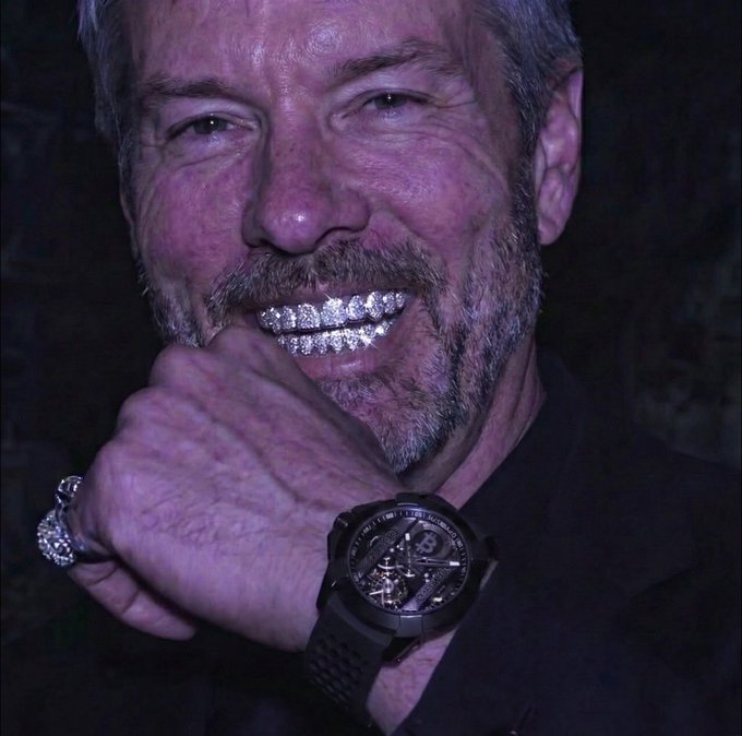 A smiling, bearded man shows off a bedazzled grill, a luxury watch with a "B" logo (likely a Breitling), and a diamond-encrusted ring, projecting an aura of opulence and success that visually complements the post's bullish claim that Strategy ($MSTR) will become the world's biggest company through its Bitcoin ($BTC)-backed credit instruments ($STRC).