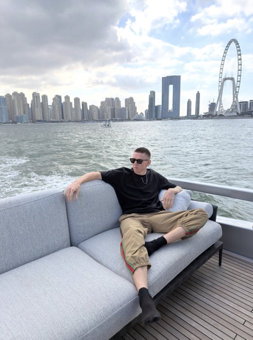 A man in sunglasses relaxes on the deck of a luxury yacht, with a skyline featuring a large Ferris wheel and modern skyscrapers visible across the water. The image reinforces the post's message about trading success—by managing risk and position size, smart money eventually earns the lifestyle of cruising in luxury rather than chasing trades.
