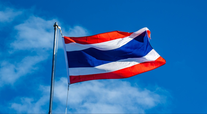 Thailand's flag waves against a partly cloudy blue sky, symbolizing the country's recent move to implement a 0% capital gains tax on Bitcoin and crypto assets—an initiative being discussed as a potential model for Indonesia to attract more investors and crypto projects.