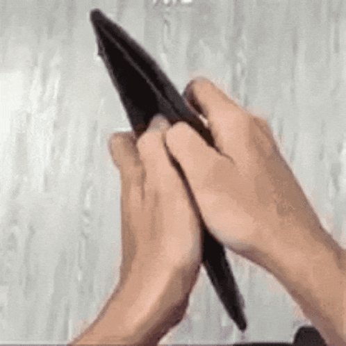 The image shows a person's hands holding an open wallet, with their fingers visible as they interact with the wallet. The wallet appears to be black and has a unique design that stands out against the white background of the photo. The person seems to be examining or opening the wallet, possibly searching for something inside it.