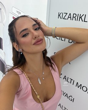 A woman with brown hair poses confidently, wearing a pink top and a silver pendant necklace, with the text "KIZARIKL" and "ALTI MO" visible on the wall behind her. The caption "Dünya’nın en güzel kadını" (the world's most beautiful woman) celebrates her striking beauty and poised expression.