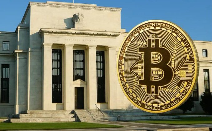 A Bitcoin coin is superimposed in front of the U.S. Federal Reserve building, symbolizing the potential impact of Fed decisions on cryptocurrency markets. The text visible on the coin reads "BITCOIN DIGITAL DECENTRALIZED PEER TO PEER CRYPTOCURRENCY 999 FINE COPPER"