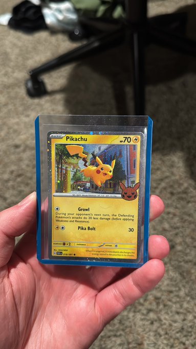 The image features a person holding a Pokemon card, specifically a Pikachu card, with their hand visible. The background of the photo shows a chair and a carpeted floor, suggesting that this scene takes place indoors. The post about Cosmos foils has been shared by someone who is interested in the game, possibly a fan or a fellow player.