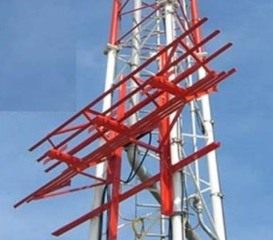 A red and white communications tower or antenna structure stands against a blue sky.