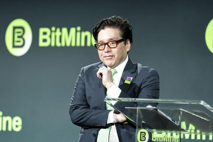 A man in a dark suit and glasses speaks at a BitMine podium, with the company's logo displayed on the screen behind him.