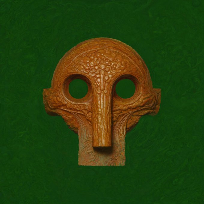 A textured, orange-brown sculptural mask or artifact featuring eye holes and intricate carved patterns, displayed against a deep green background.