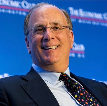 A smiling, bespectacled older man in a dark suit and colorful polka-dot tie appears to be on stage at an Economic Club event, with partial text reading "ECONOMIC" and "Club" visible on the backdrop behind him—likely Larry Fink, CEO of BlackRock.