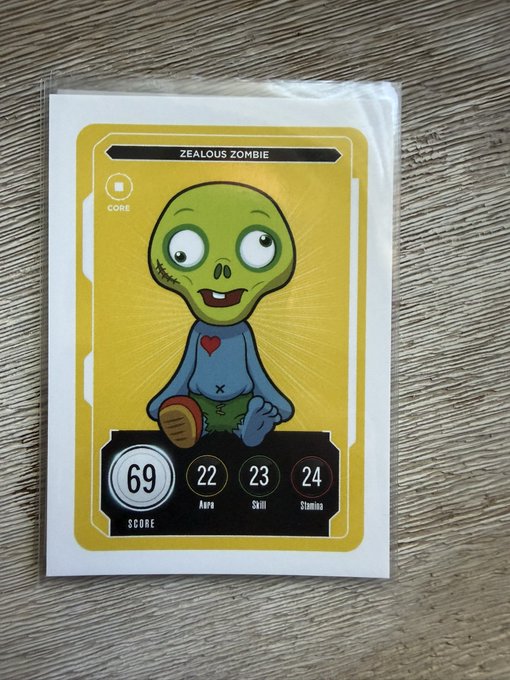 A trading card in a plastic sleeve labeled 'ZEALOUS ZOMBIE' featuring a green zombie character with stats: Score 69, Aura 22, Skill 23, Stamina 24.