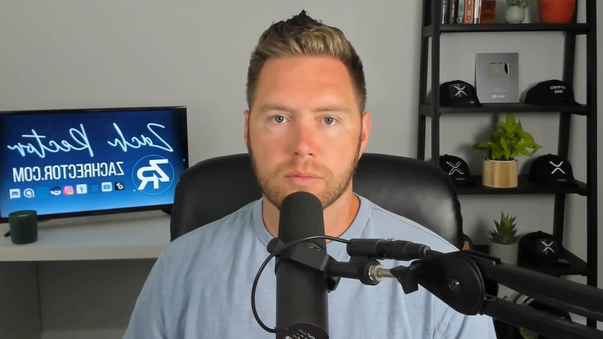 The image features a man wearing a blue shirt sitting behind a microphone, likely preparing to host or participate in an online radio show. He appears to be focused on the camera while holding the microphone close to his mouth. The background of the image includes a TV screen and several potted plants placed around the room. There is also a sign that reads "Ready for the real XRP Supply Shock?". This suggests that the man might be discussing or talking about the recent introduction of Ripple XRP, which has caused an economic shock in the cryptocurrency market.