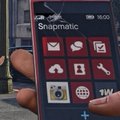 A close-up of a hand holding a smartphone displaying the 'Snapmatic' menu in a video game interface.