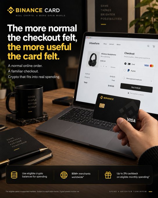 A hand holds a Binance Visa card near a laptop displaying a checkout page for UrbanForm wireless headphones priced at $169.00, alongside a black mug reading "Good People Better Money" and a notebook labeled "Spend Everyday Further Tomorrow," visually reinforcing the caption's theme of using Binance Card for a routine online purchase with up to 3% cashback on eligible crypto spending.
