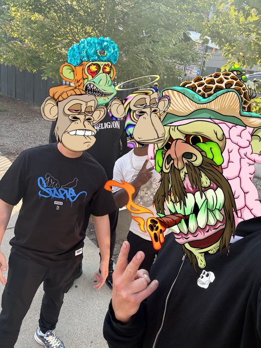 A group of people wearing colorful, cartoonish NFT-style masks (Bored Apes, etc.) posing outdoors, with one person flashing a peace sign.