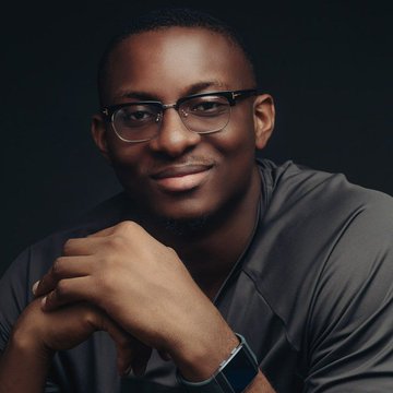 A portrait of a smiling man with glasses, wearing a dark shirt and a smartwatch.