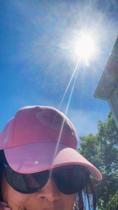 The image features a woman wearing sunglasses, a pink hat with a logo, and smiling at the camera. The background of the photo shows a blue sky and trees, creating an outdoor setting. The caption of the image includes details about upcoming events such as the NYC Tech Week conference next month and a meetup for @DestefanosSteak.