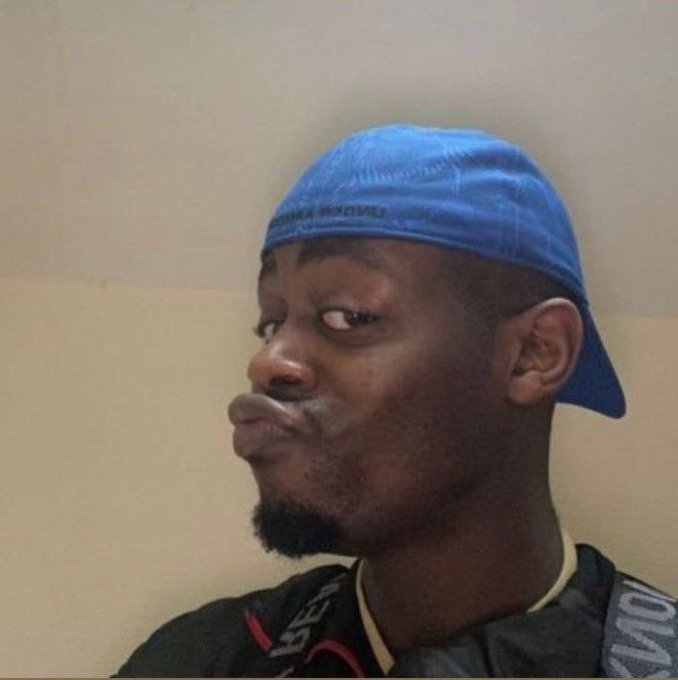 A man wearing a blue baseball cap worn backwards, with a skeptical expression, looking sideways.