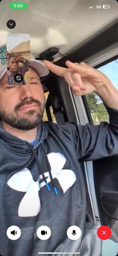 The image shows a FaceTime call with a man wearing an Under Armour hoodie in a vehicle, while a smaller inset displays another person making a peace sign. The man's hand is raised, possibly mirroring the gesture, suggesting a casual, friendly interaction that fits the post's laid-back vibe about enjoying work and crypto culture.