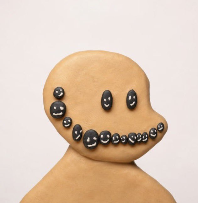 A bald, faceless clay figurine with small black smiling face-shaped protrusions arranged across its head and jaw, humorously matching the caption's reference to being bald by suggesting the figure has a "face" made entirely of tiny smiles where hair would normally grow.