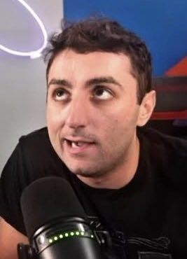 A man with dark hair and a black shirt speaks into a microphone, appearing serious as he reacts to breaking news that the token ticker "RASMR" has declined over $1.1 million in value during the past 30 days. His concerned expression suggests he is likely a crypto commentator or influencer covering the significant market downturn.