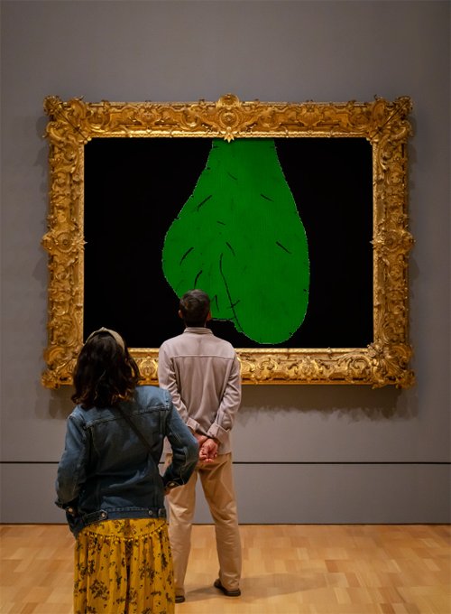 A couple stands in a museum gazing at a large contemporary artwork featuring an ornate gold frame surrounding a black background with a green pear-shaped form, reminiscent of Magritte's style.