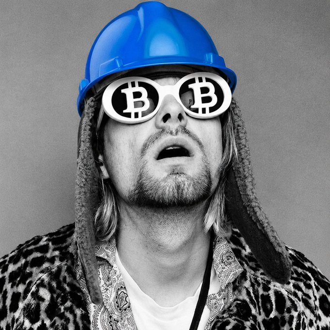 A stylized black-and-white portrait of a man with long hair and a goatee, wearing a blue hard hat and oversized sunglasses featuring the Bitcoin "₿" logo on each lens, paired with a leopard-print jacket. The image humorously reinterprets a meme-style photo with crypto-themed accessories, playfully visualizing how the trader @cobie might appear if he were actively trading on the @baseapp platform.