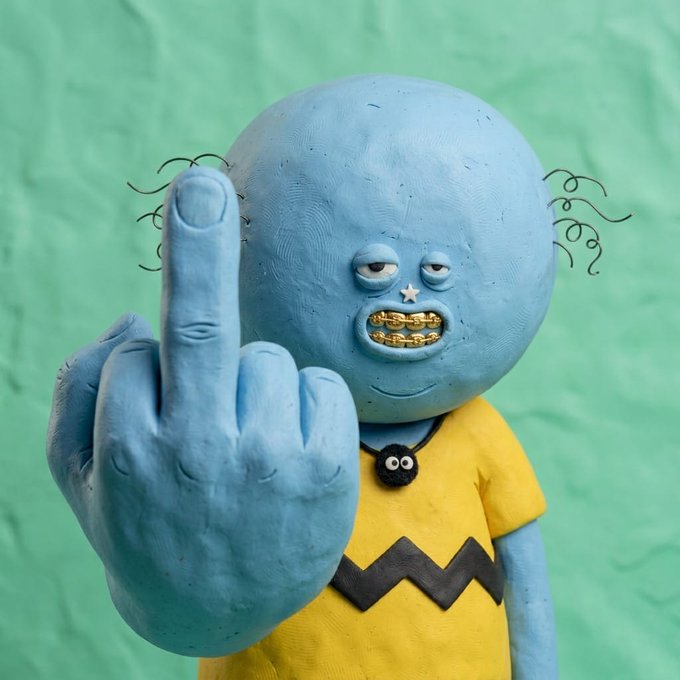 The image features a blue clay sculpture of a cartoon character, possibly a cartoon monster or a character from a popular TV show like "The Simpsons." The sculpture has a yellow shirt with black stripes and a black and white cat's face on its head. It is making an offensive gesture by giving the middle finger, which is typically associated with dislike or disapproval in human culture. The sculpture is placed against a green background, creating a contrast that highlights its unique design.