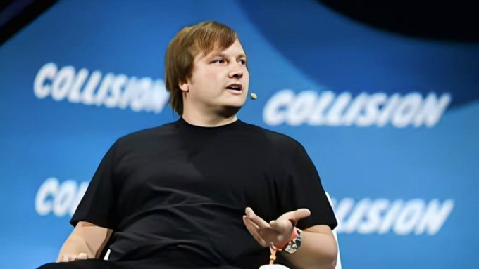 A man wearing a black t-shirt speaking on stage at the Collision conference.