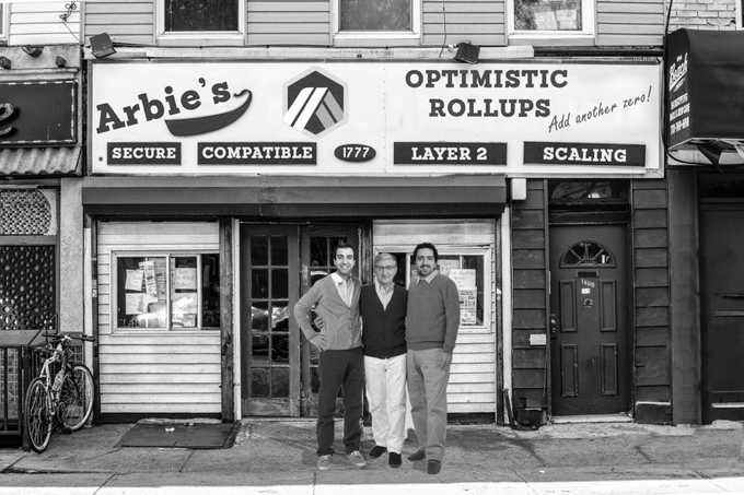 Three men stand in front of a storefront with a sign reading "Arbie's Optimistic Rollups," featuring tags "Secure, Compatible, Layer 2, Scaling" and "1777," in a black-and-white photo marking Arbitrum's 5th birthday at the Princeton location where the project began.