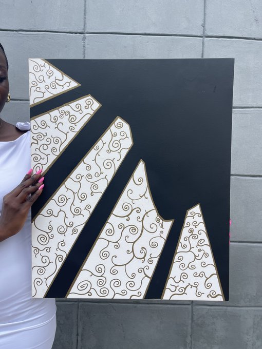 A person holds a large black and white abstract canvas artwork featuring ornate swirl patterns and geometric shapes against a gray cinderblock wall.
