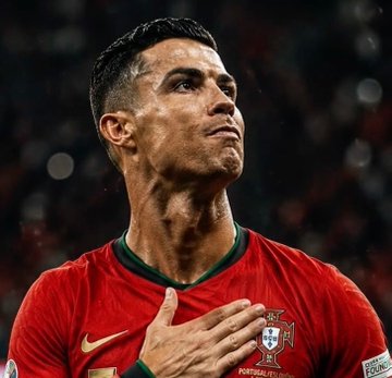 The image shows Cristiano Ronaldo wearing Portugal's red national team jersey, with his hand placed over his chest and the Portuguese national team crest visible, as he appears to be looking upward in a solemn or reflective moment during a match. The image relates to the post as it depicts Ronaldo in action for Portugal against Spain, the very match referenced in the Polymarket betting news about whether he would score.