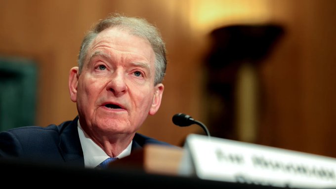 A nameplate reading "Hon. [Senator] Chairman" sits before a microphone as an older man in a dark suit speaks during what appears to be a congressional hearing. The image connects to the post's news about the SEC preparing crypto regulations, likely depicting a Senate Banking Committee chairman discussing potential financial oversight.