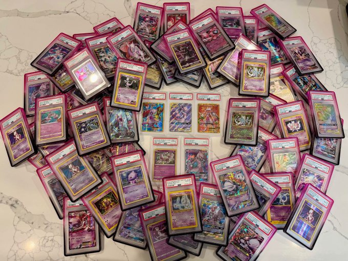Large collection of Pokémon trading cards spread out on a white marble surface, featuring many holographic and rare cards in protective sleeves.
