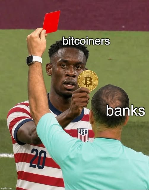 A soccer referee shows a red card to a USA player holding a Bitcoin coin, with the referee labeled "banks" and the player labeled "bitcoiners," symbolizing the clash between Bitcoin's capped 21 million supply and traditional banking systems.